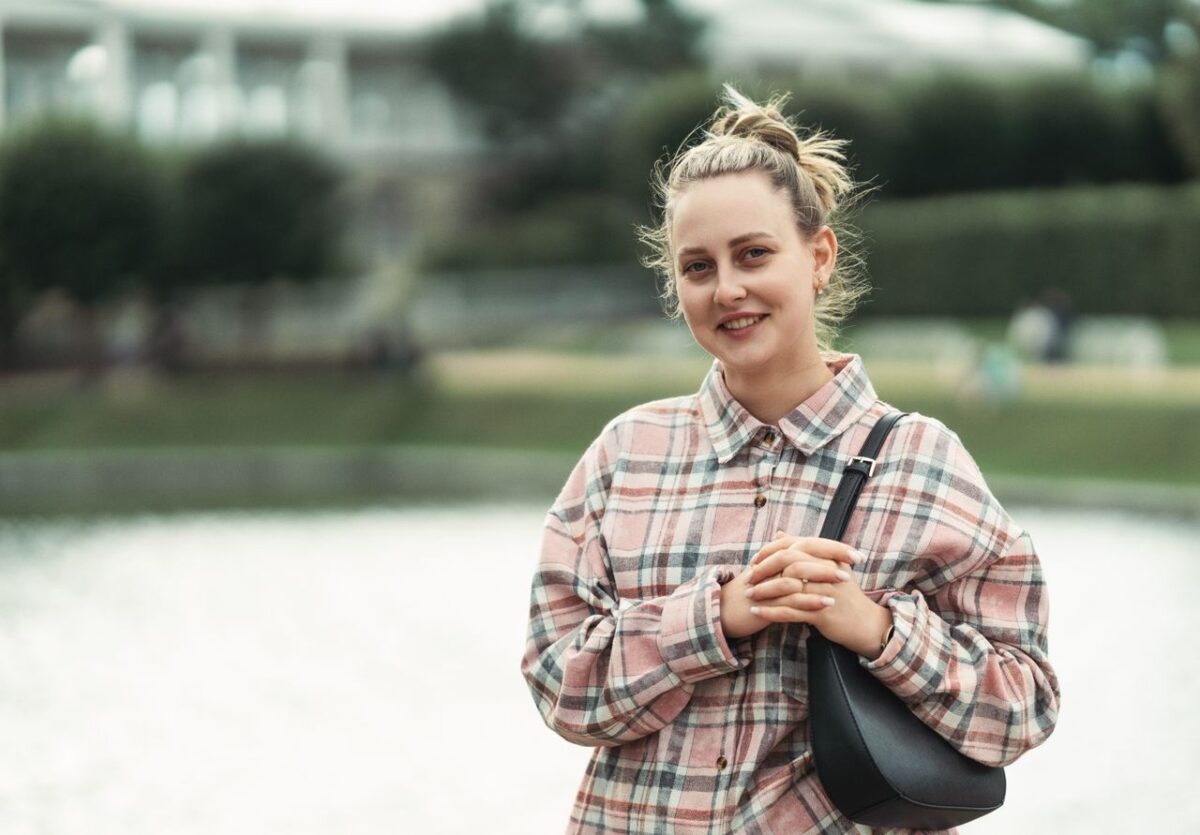 Respect et Charisme A woman in casual attire standing by a lake smiling outdoors, conveying a relaxed mood.