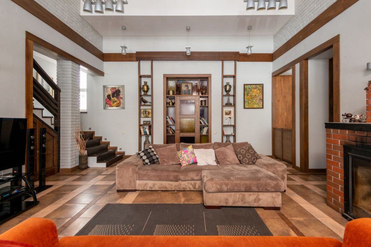 À propos Interior of modern apartment with comfortable sofa and decorative elements on wooden shelves at wall in room with staircase and brick fireplace
